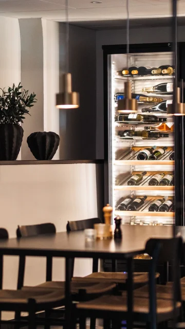 Hotellets chambre separee med svart bord och svarta stolar, vinkylar med vin samt svara dekorativa krukor